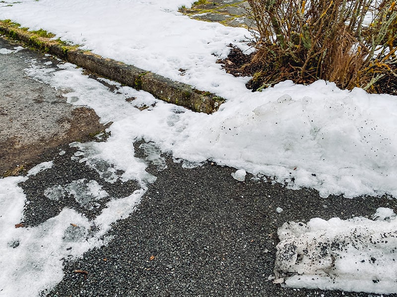 A wheelchair ramp covered in compacted snow and ice, its handrail and surface indistinguishable from the ground beside it.