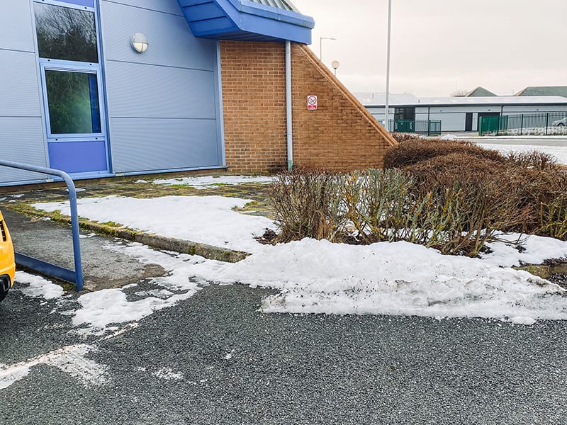 Snow cleared from a car park and piled directly across a building's entrance and its dropped kerb.